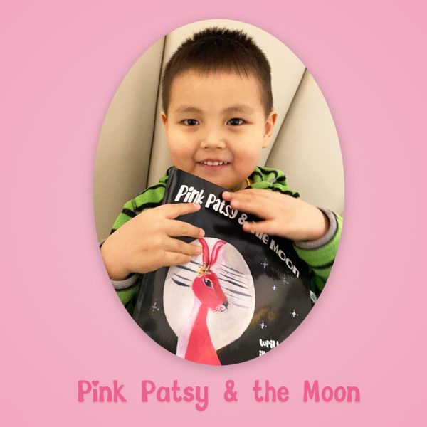 Young child smiling while holding a copy of Pink Patsy and the Moon.