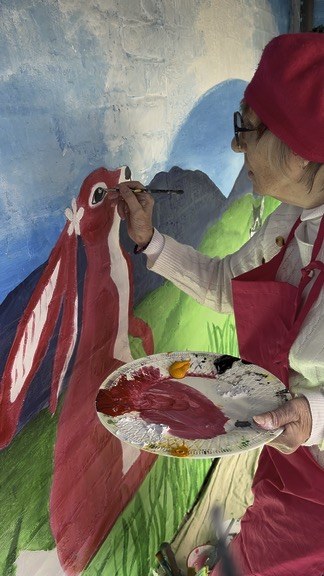 Margaret holding her palette and painting Pink Patsy’s eye on the Crocodile Café mural