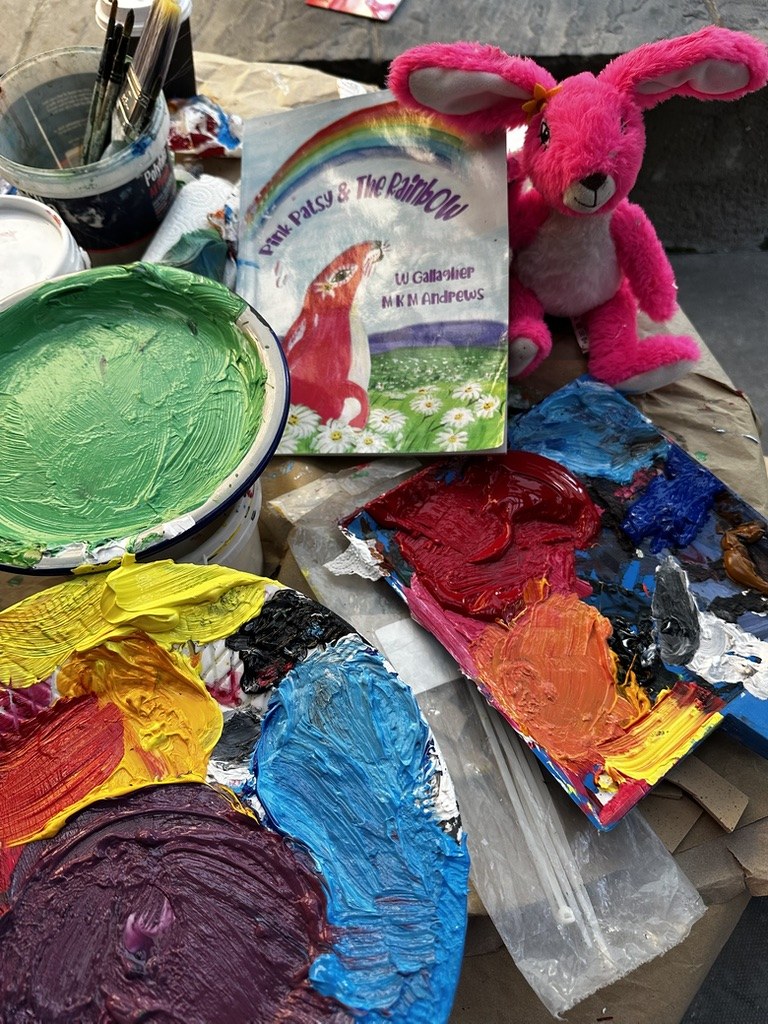 Palettes of bright paint, brushes, the Pink Patsy and the Rainbow book and a Pink Patsy teddy on the mural painting table
