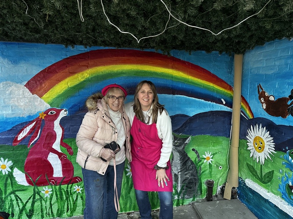 Margaret and a member of the Pink Patsy team in front of the finished Pink Patsy rainbow mural at the Crocodile Café in Muswell Hill