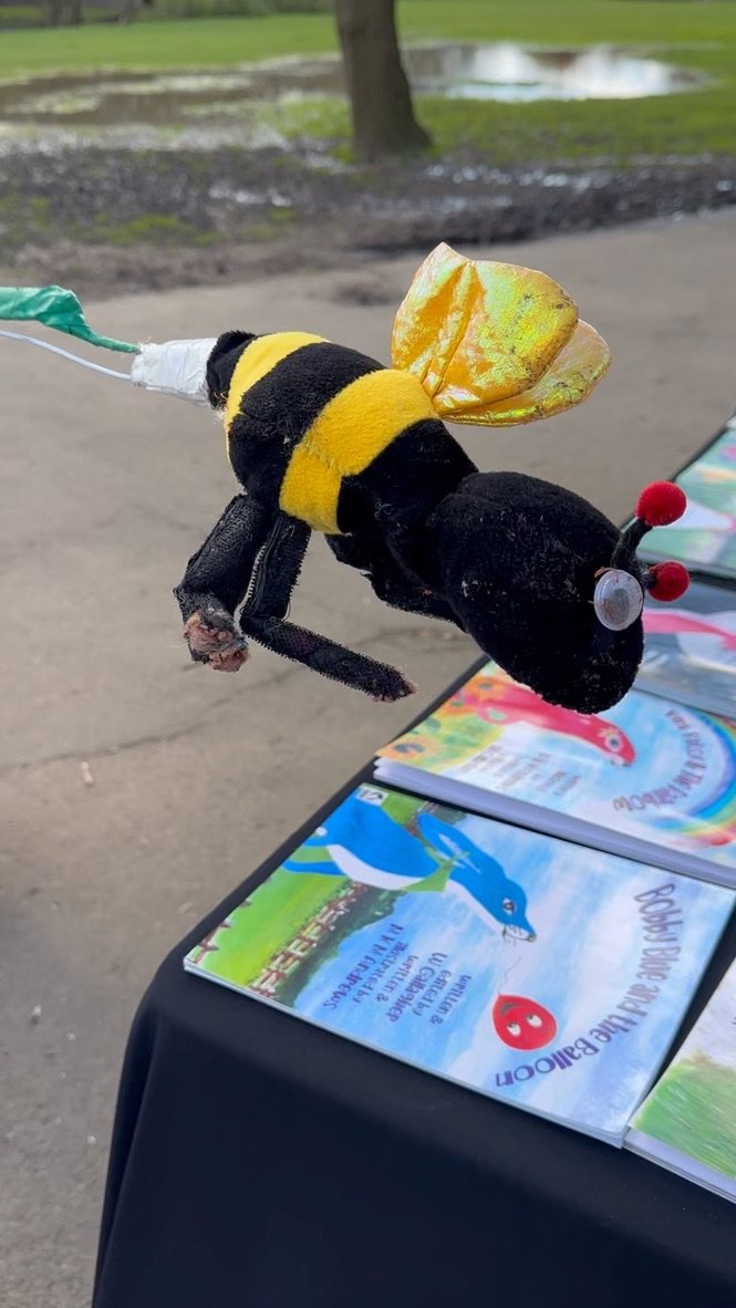 Jake's fluffy bee puppet with shiny gold wings flying over a table of Pink Patsy and Bobby Blue books