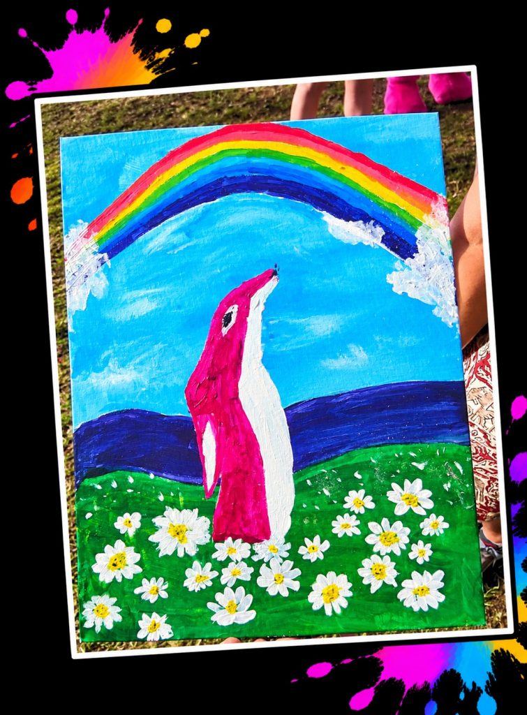 A beautiful painting of Pink Patsy gazing up at a rainbow over a meadow full of daisies, made at a Painting in the Park event