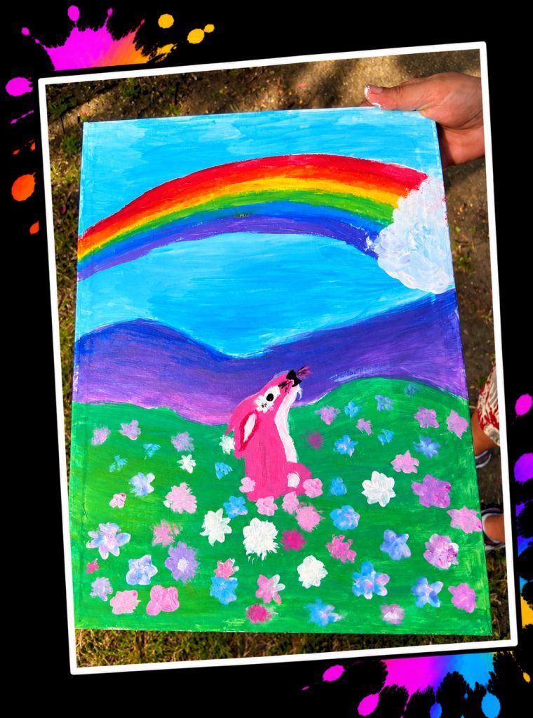 A painting of Pink Patsy sitting in a meadow of pink, blue and white flowers beneath a rainbow, made at a Painting in the Park event