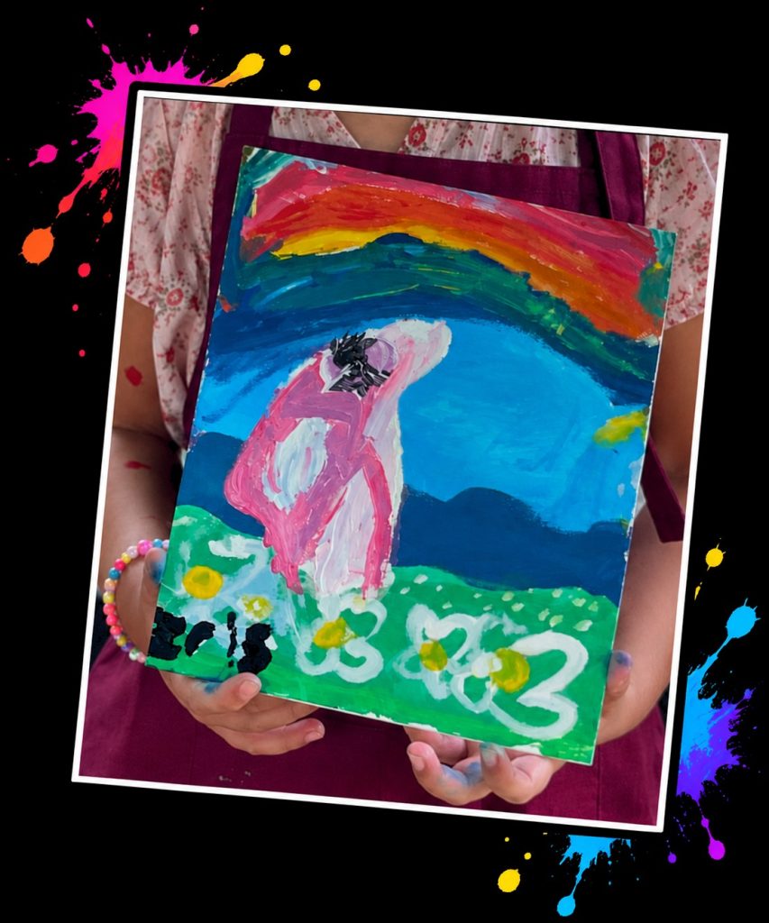 A child’s painting of Pink Patsy under a rainbow, made at a Painting in the Park with Pink Patsy event