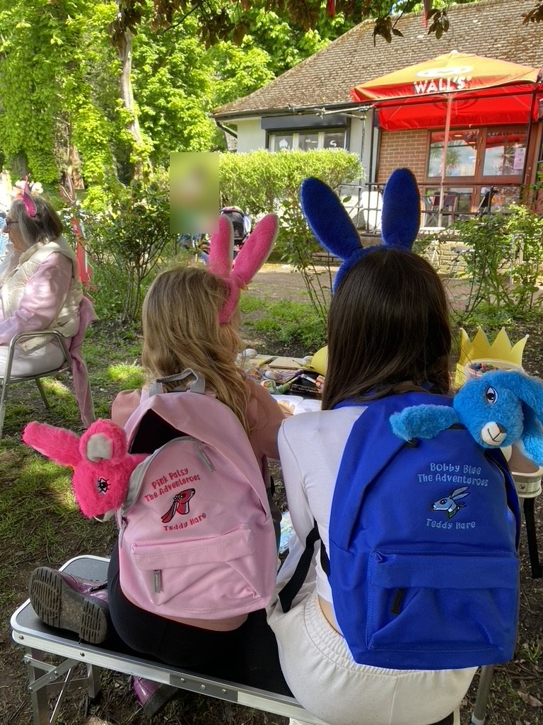 Two children with Pink Patsy and Bobby Blue Adventure Pack rucksacks at an outdoor craft table