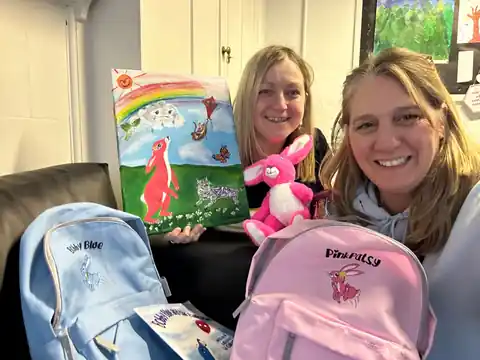 Wendy with Mrs Goodwin of Barnfield School holding a Pink Patsy painting, teddy, adventure backpacks and books